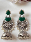 Pair of oxidised silver jhumka earrings with green stones and pearl fringe laid flat on white surface