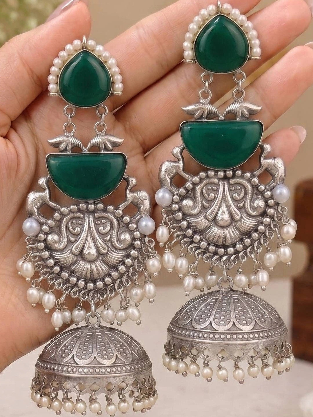 Both jhumka earrings held in open palm showing full three-tier design with dome bell and pearl drops