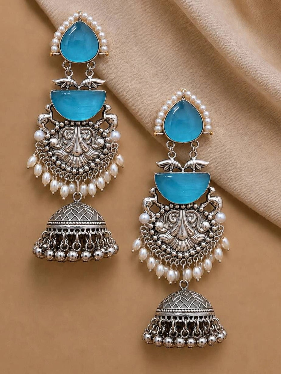 Pair of blue stone oxidised silver jhumka earrings laid flat on beige fabric