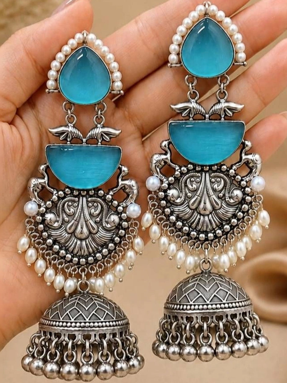 Pair of oxidised silver jhumka earrings with blue stones and pearl fringe held in open palm