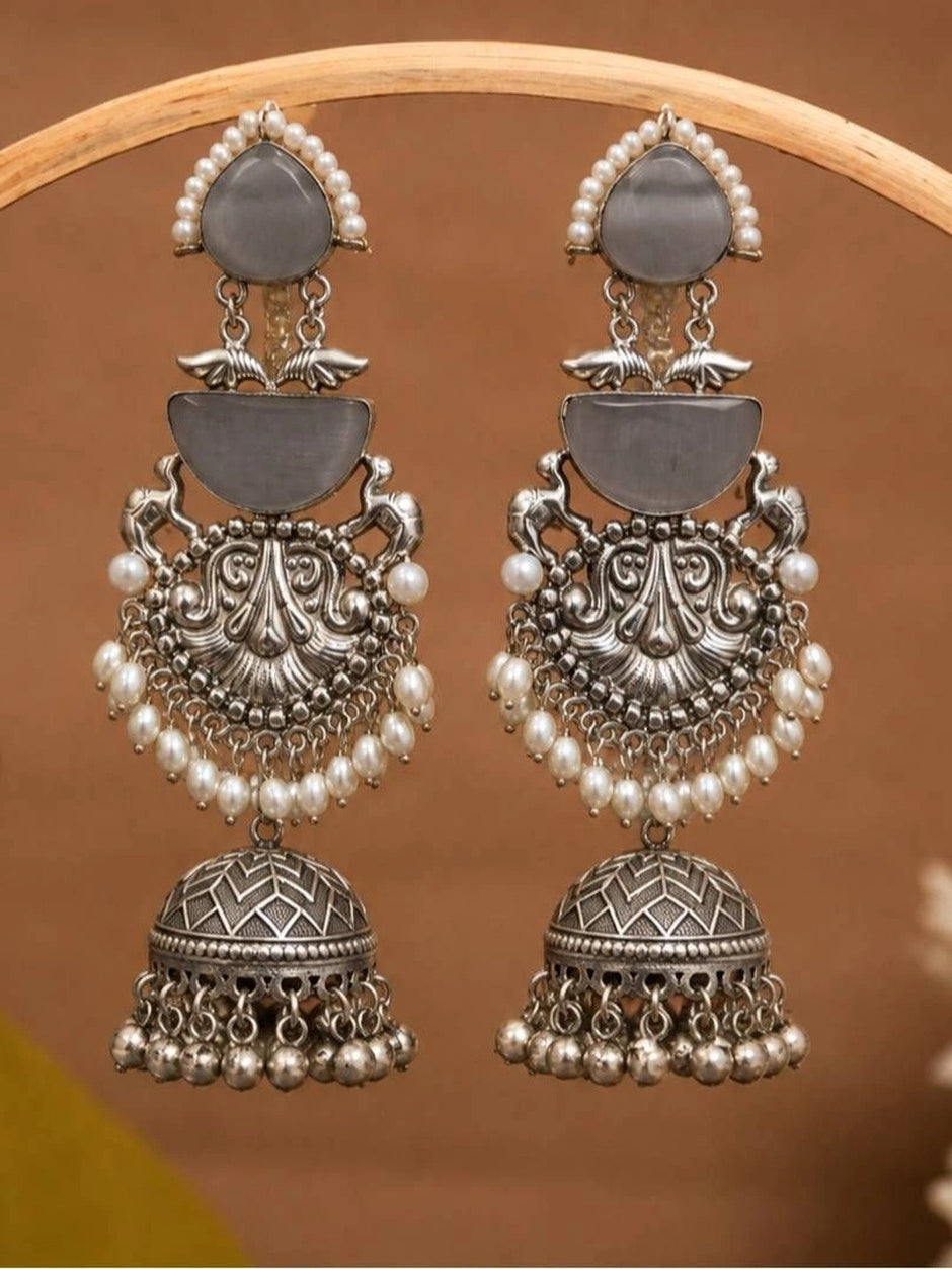 Pair of oxidised silver jhumka earrings with grey cat-eye stones and pearl drops displayed on a wooden ring stand
