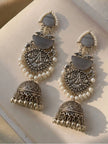 Two oxidised silver layered jhumka earrings laid flat on a cream surface showing full design detail