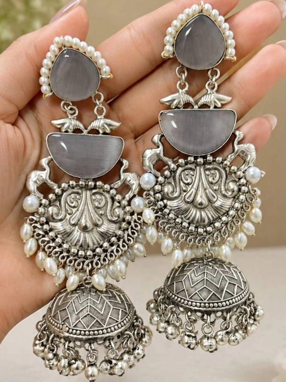 Both oxidised silver jhumka earrings held in a woman's open palm showing full length and layered detail