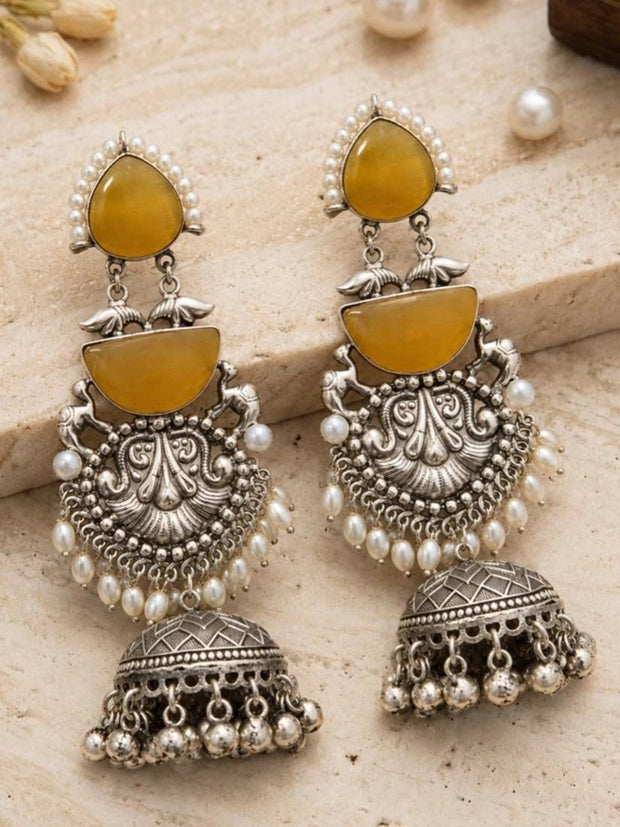Pair of oxidised silver chandbali jhumka earrings laid flat on a cream textured surface with pearls nearby
