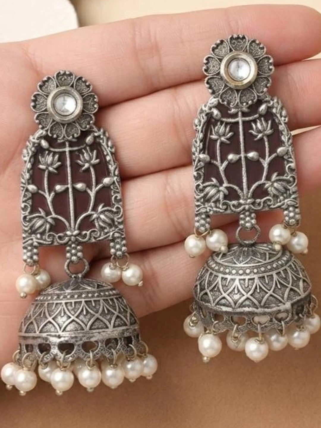 Close-up of lotus jhumka earring pair held in palm showing engraved dome and pearl drops