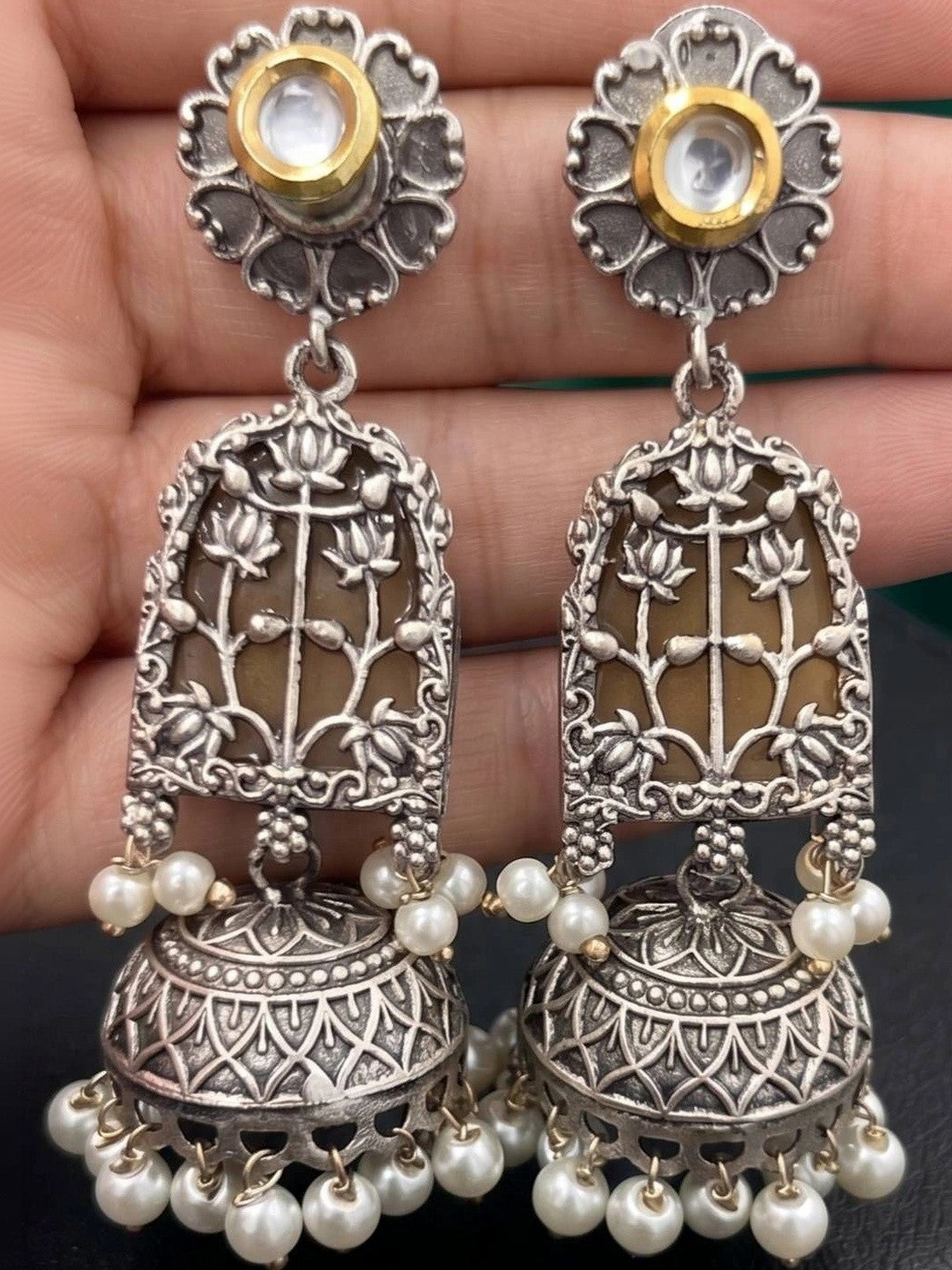 Pair of oxidised silver lotus jhumka earrings with kundan tops and pearl drops held in a hand