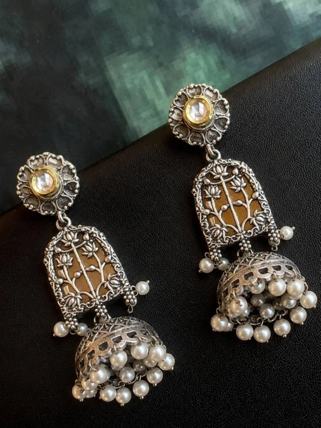 Oxidised silver jhumka earrings lying flat showing lotus filigree arch and pearl bead fringe