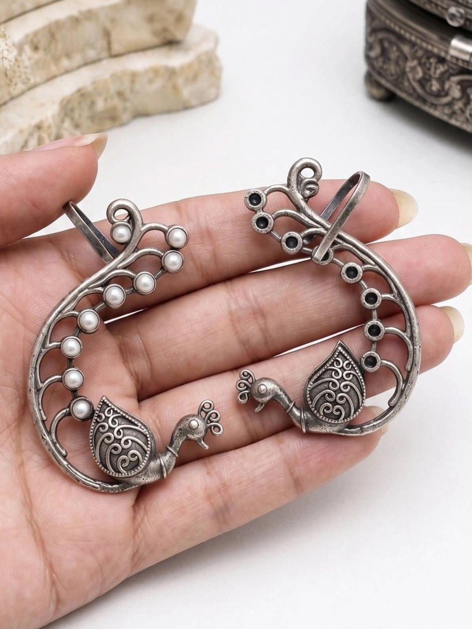 Pair of peacock ear cuffs side by side on white surface showing bar fastening and stone accents
