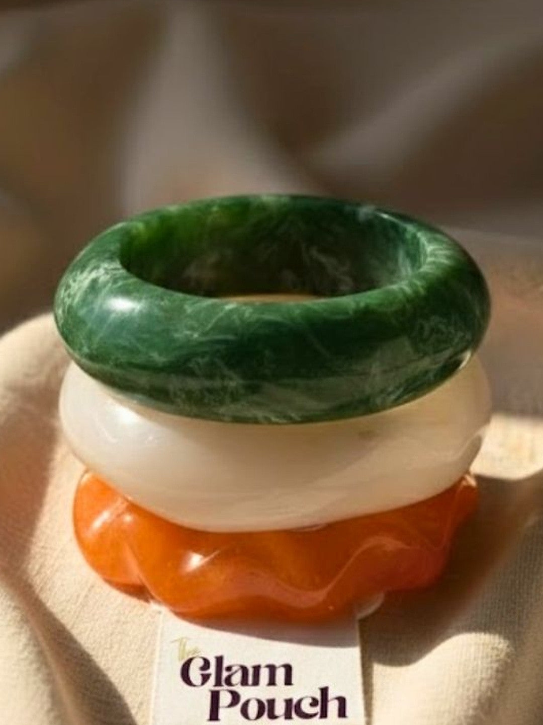 Close-up of green, white and orange marble resin bangles stacked on a linen pouch card