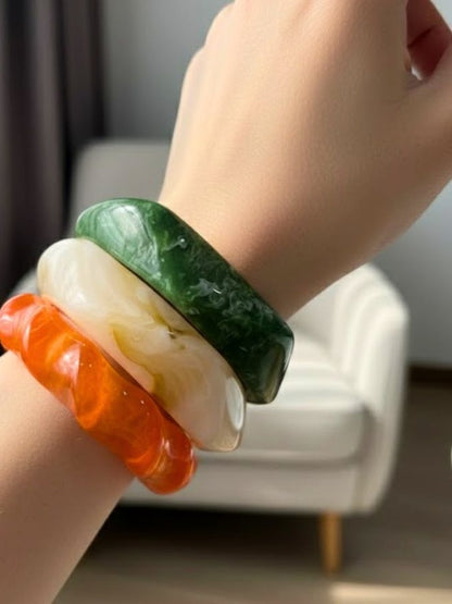 Green marble, ivory white and orange resin bangles worn stacked on a woman's wrist