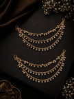 Two gold-plated layered pearl ear chains displayed on a dark black surface with baby's breath flowers