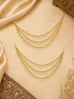 Pair of gold-plated pearl drop ear chains laid on cream satin fabric beside ornate brass decor