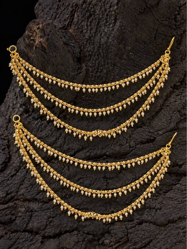 Two gold-plated pearl ear chains displayed in arc shape against dark wood bark