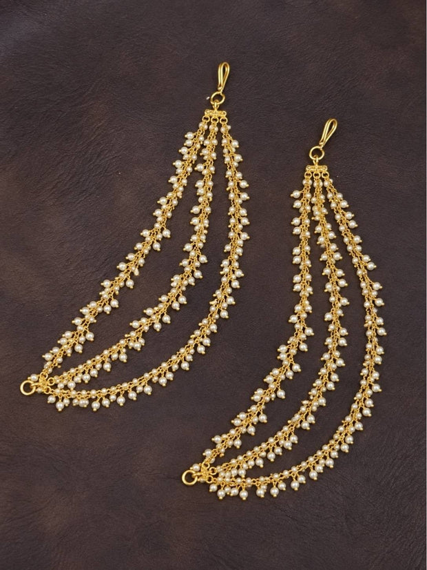 Pair of gold and seed pearl three-strand ear chains laid flat on dark leather surface