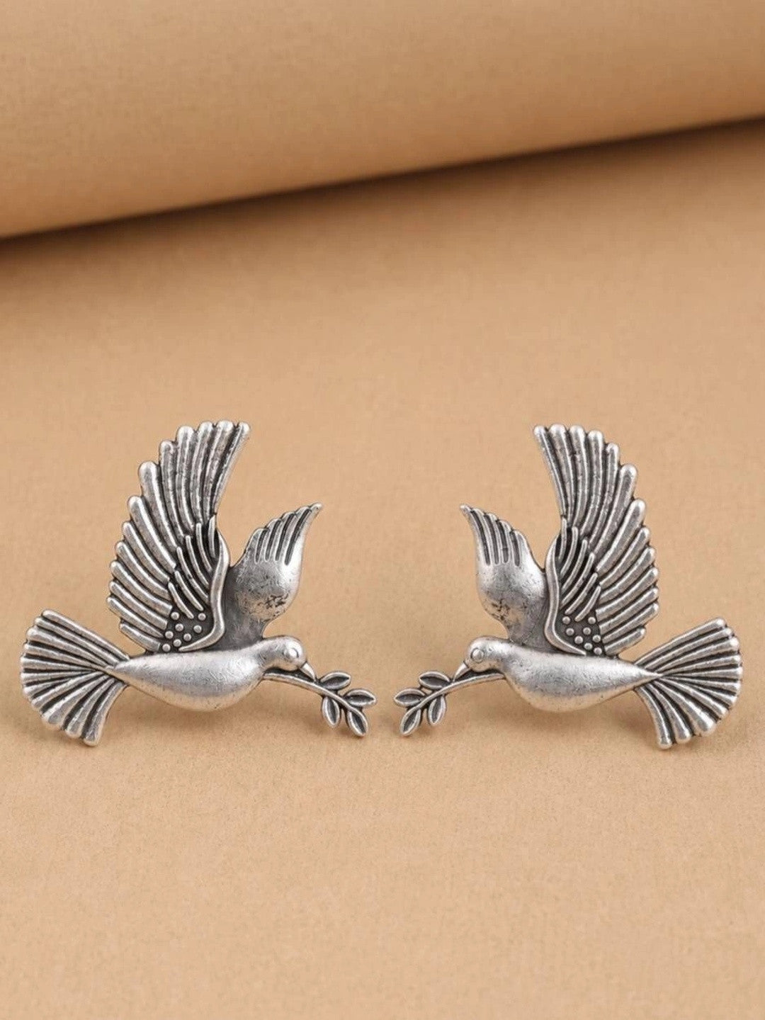 Two oxidised silver dove studs facing each other on beige background showing feather detail