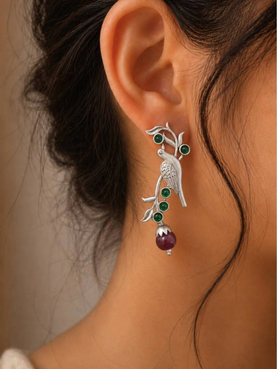 Oxidised silver parrot drop earring worn on a woman's ear with green stones and burgundy bead