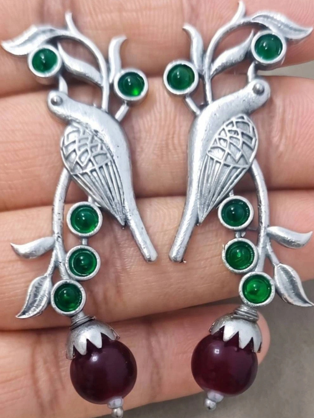 Close-up of both parrot earrings held in palm showing etched bird body and green stone embellishments