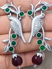 Close-up of both parrot earrings held in palm showing etched bird body and green stone embellishments