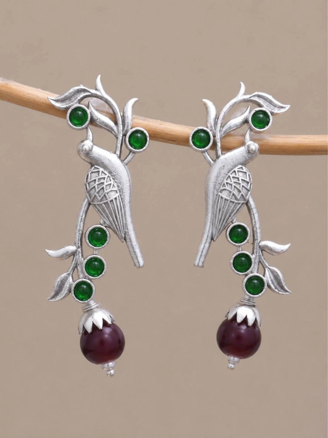 Pair of oxidised silver bird drop earrings hanging from a wooden rod against a neutral background