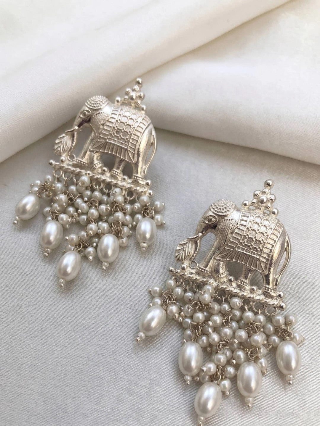 Two oxidised silver elephant earrings laid flat on white fabric showing pearl drop detail from the front