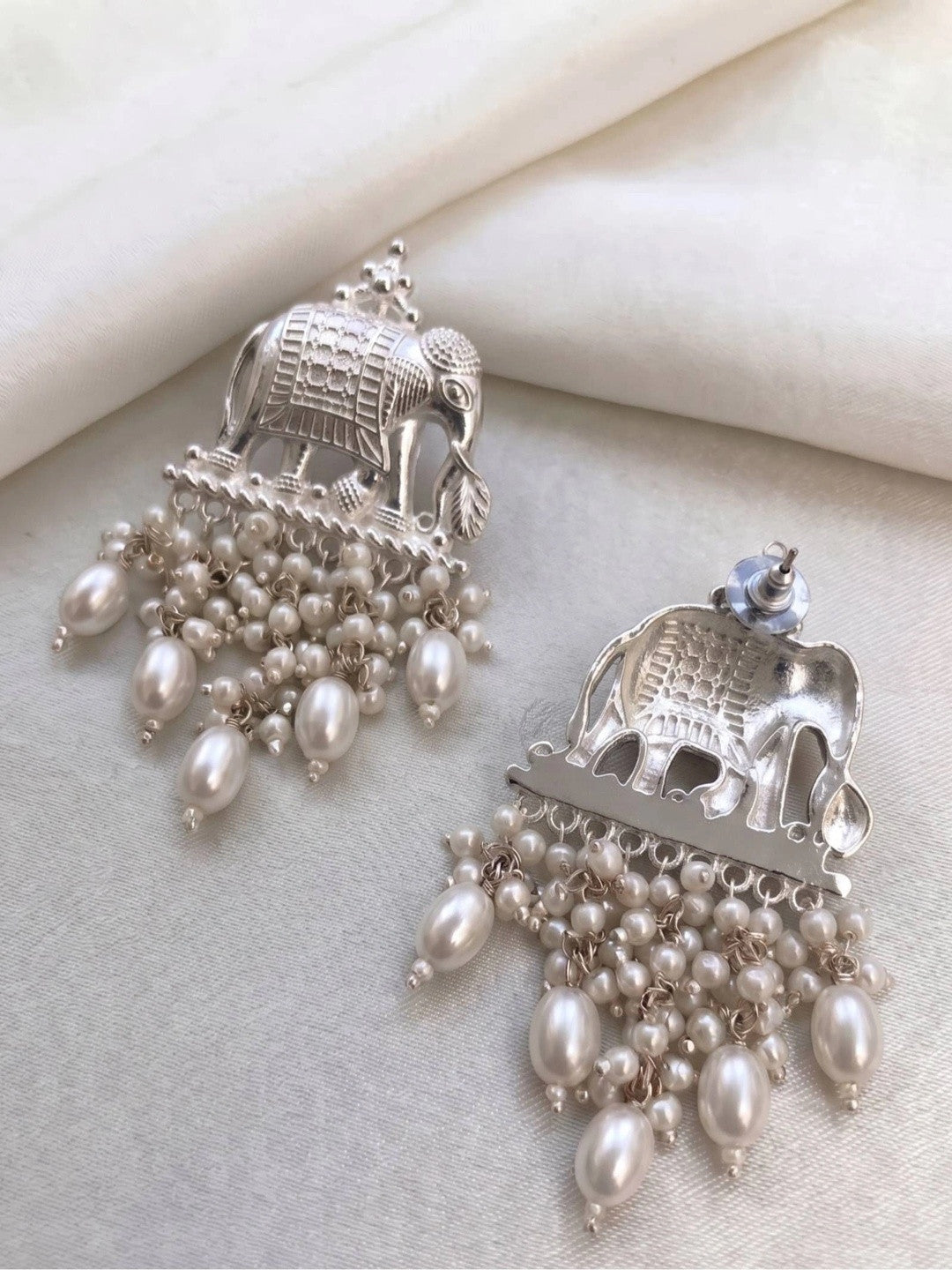 Front and back view of elephant earrings on white fabric showing stud post fastening and faux pearl drops