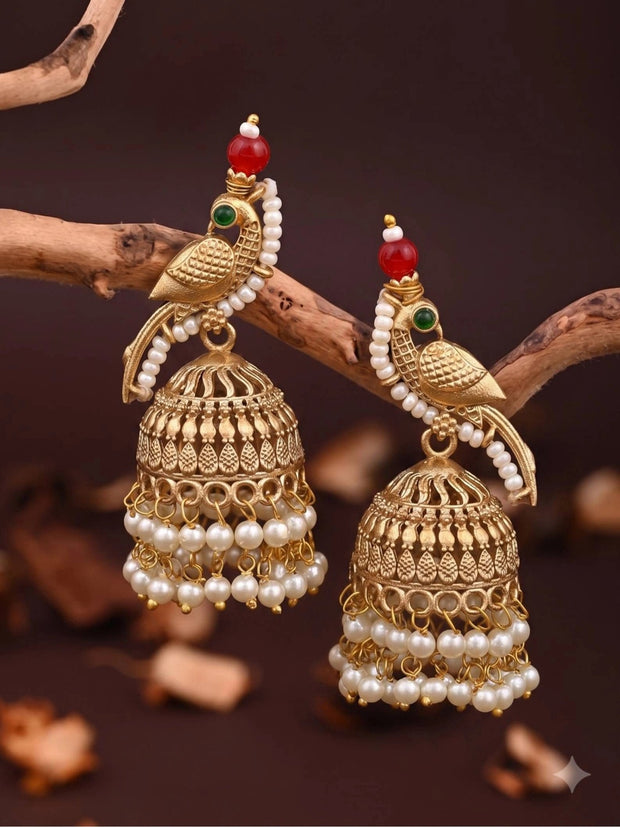 Pair of gold-plated parrot jhumka earrings with pearl drops resting on a wooden branch against dark background