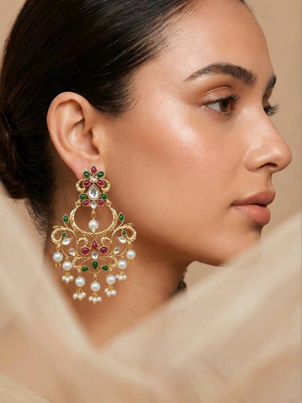 Model wearing a large gold-plated kundan chandbali earring with red and green stones and pearl drops, side profile view
