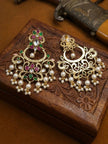 Pair of gold-plated kundan chandbali earrings laid flat on a carved wooden box, front and back sides visible