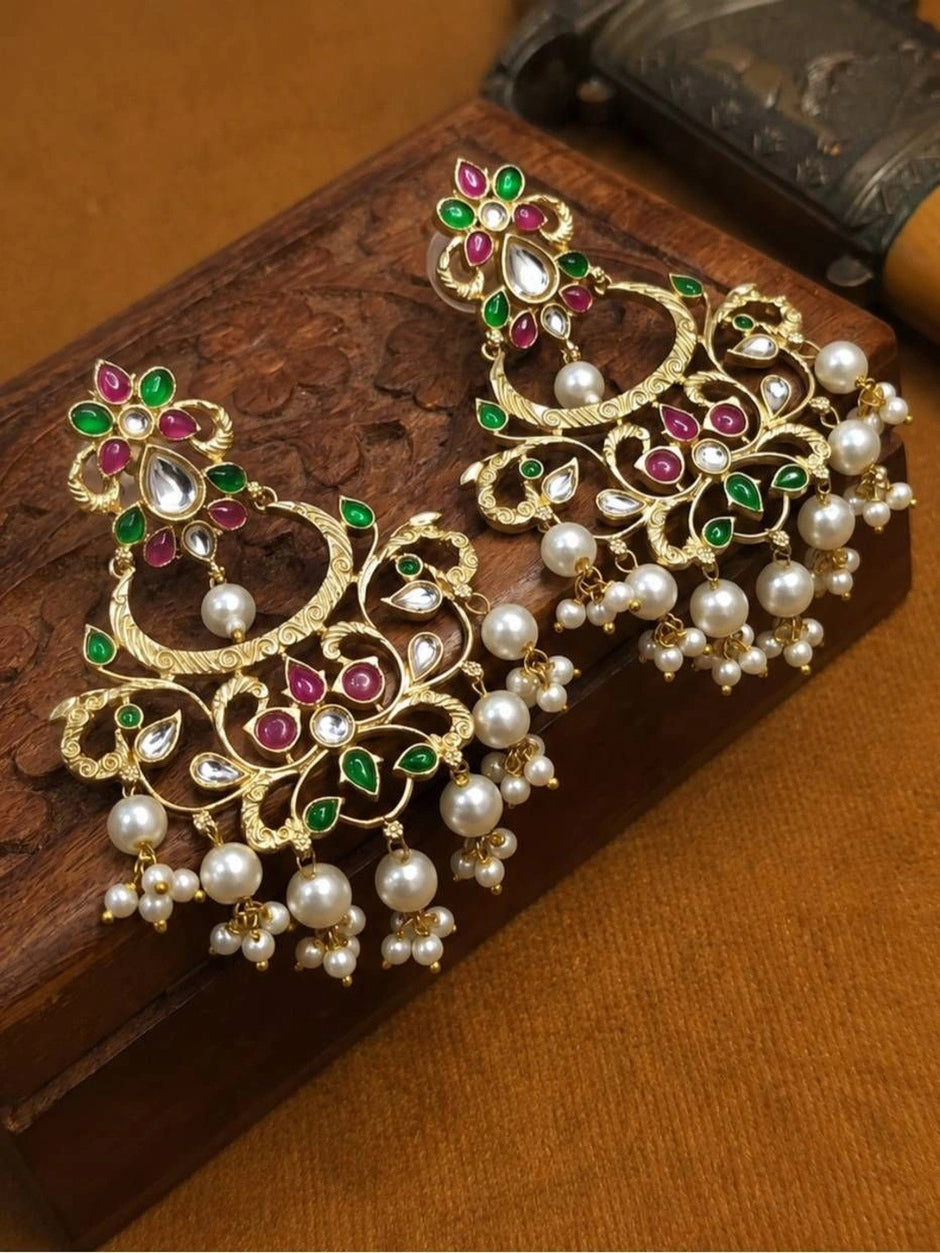 Two gold-plated chandbali earrings with kundan and pearl drops resting on a carved wooden surface at an angle