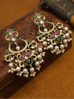 Two gold-plated chandbali earrings with kundan and pearl drops resting on a carved wooden surface at an angle