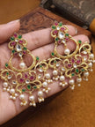 Close-up of gold-plated kundan chandbali earrings held in a palm showing scrollwork, coloured stones and cascading pearl drops