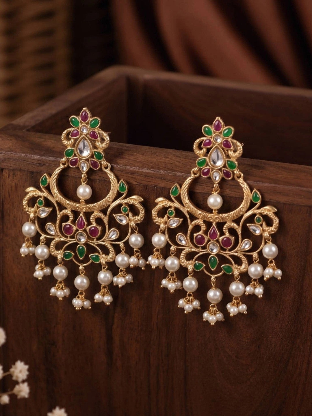Pair of gold-plated kundan chandbali earrings with floral top and pearl fringe displayed upright in a wooden box