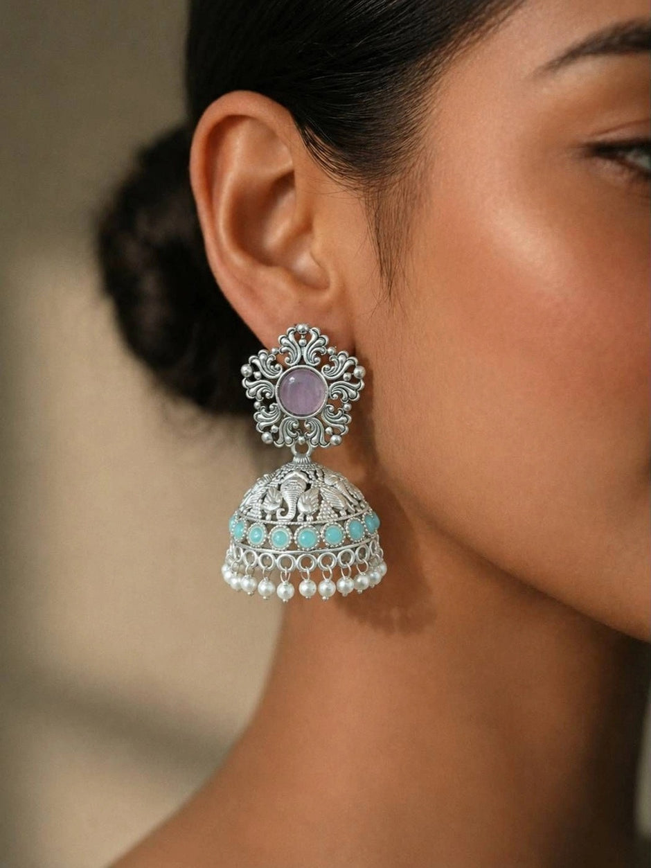 Oxidised silver elephant jhumka earring worn on model's ear showing lavender stud top and turquoise bead trim with pearl drops
