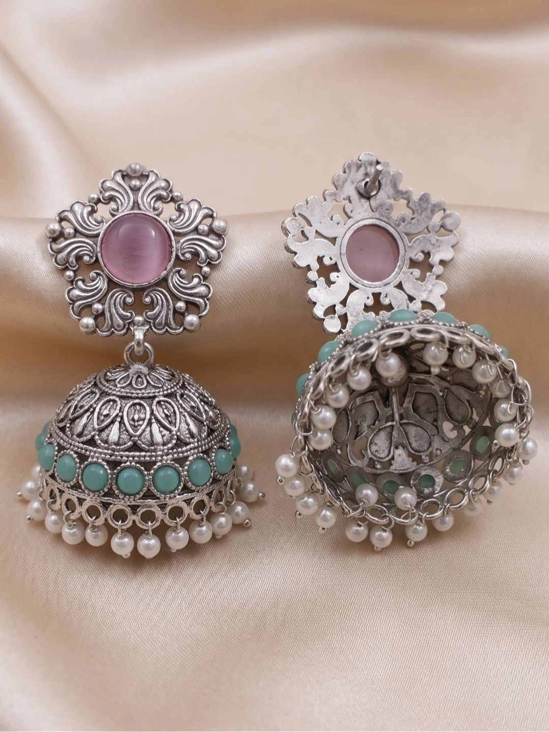 Front and back view of oxidised silver jhumka earrings on cream fabric showing scrollwork stud and pearl drop hem