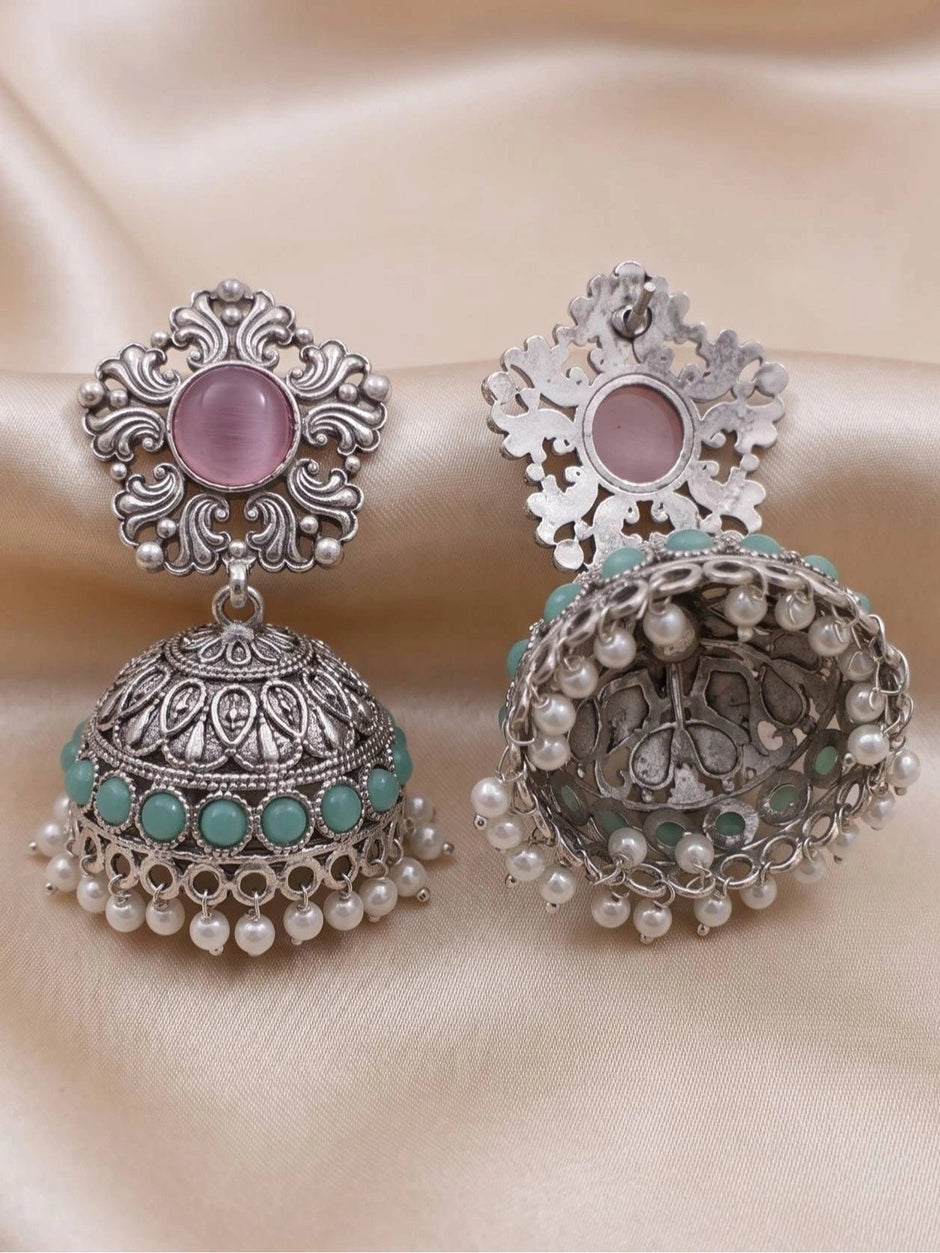 Front and back view of oxidised silver jhumka earrings on cream fabric showing scrollwork stud and pearl drop hem