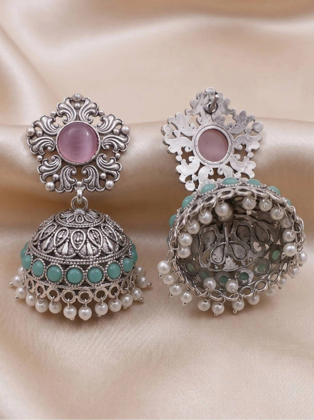 Front and back view of oxidised silver jhumka earrings on cream fabric showing scrollwork stud and pearl drop hem