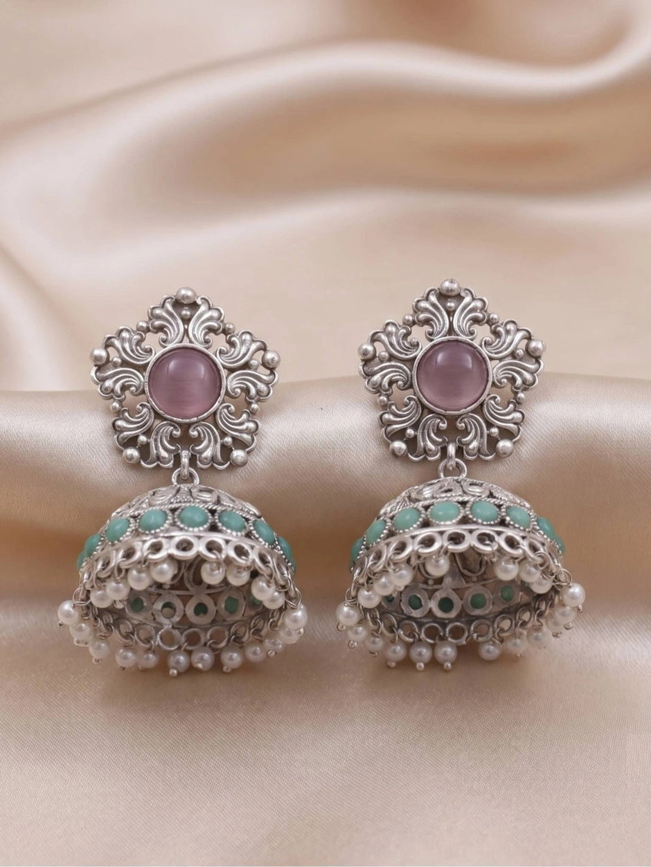 Pair of oxidised silver jhumka earrings laid flat on cream satin showing turquoise bead row and pearl fringe detail