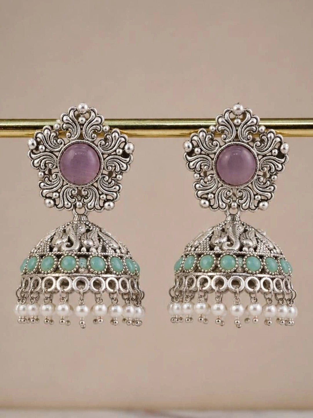 Pair of oxidised silver elephant jhumka earrings hanging from a gold rod showing full silhouette with pearl drop fringe