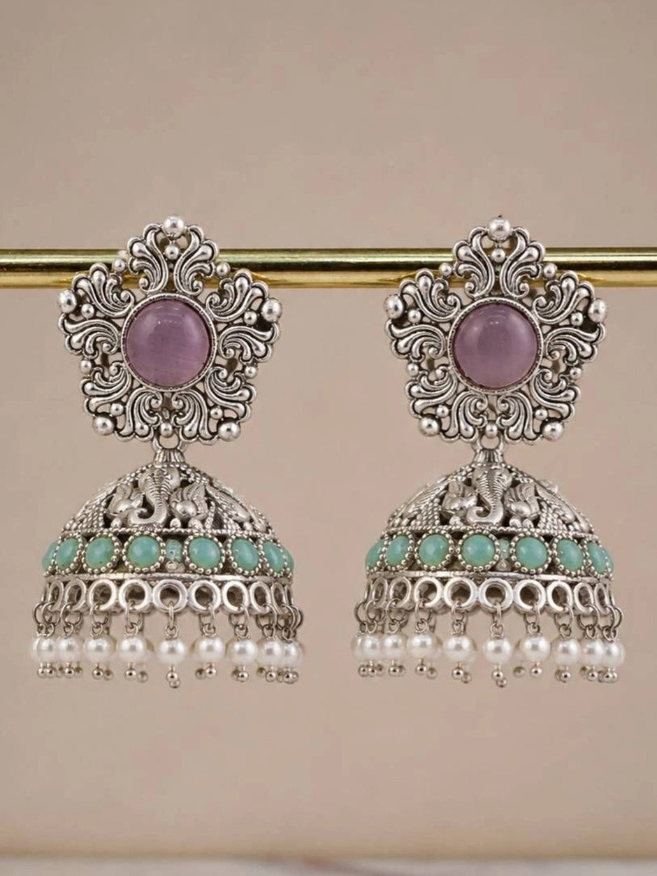 Pair of oxidised silver elephant jhumka earrings hanging from a gold rod showing full silhouette with pearl drop fringe