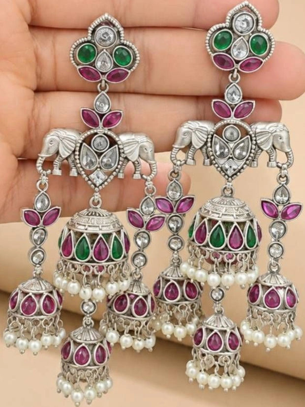 Pair of oxidised silver elephant jhumka earrings held in hand showing ruby green stones and pearl drops