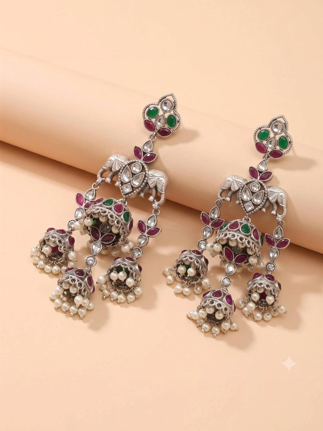 Two oxidised silver elephant jhumka earrings laid flat on beige surface showing full length and detail