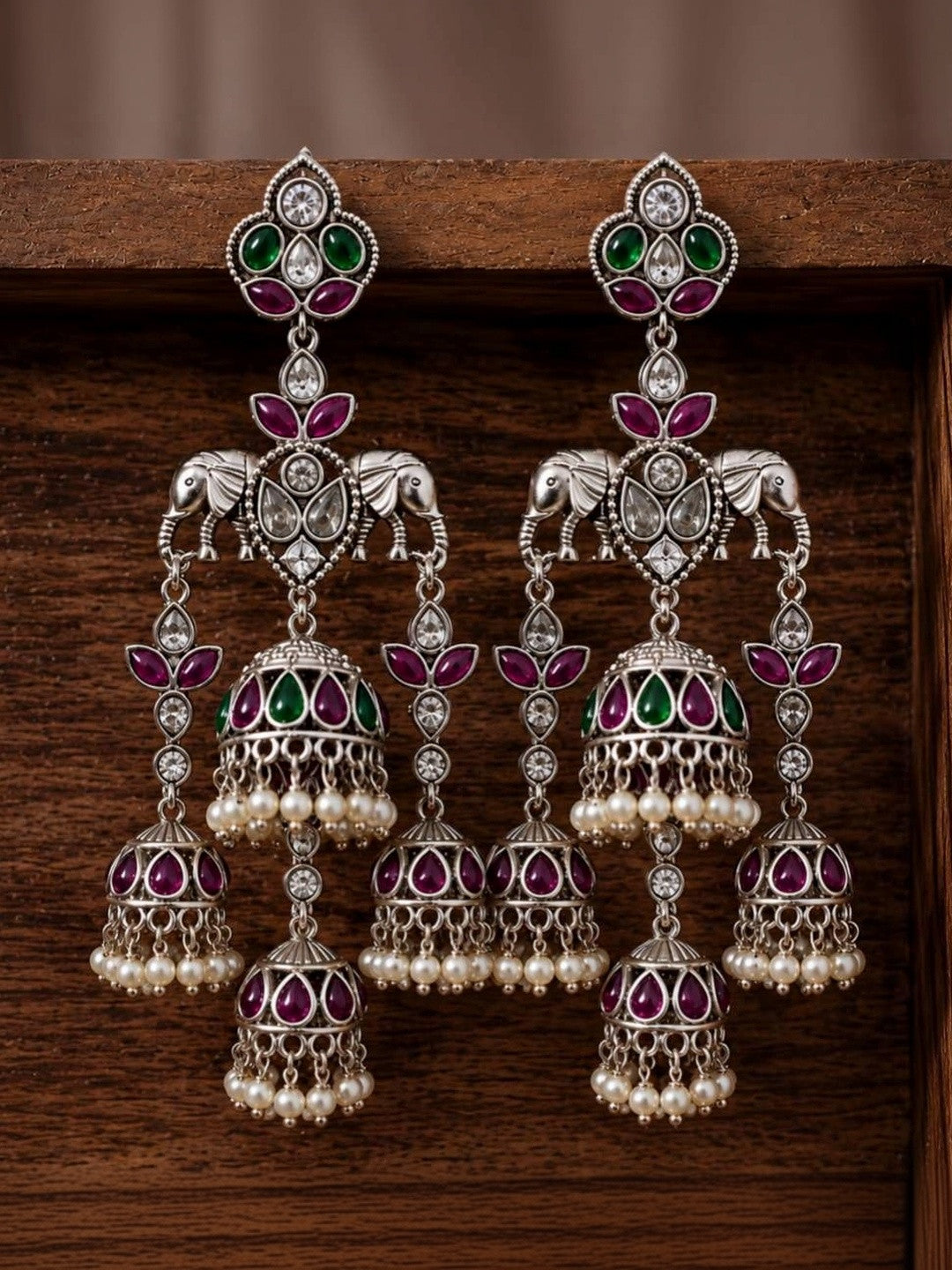 Pair of oxidised silver triple jhumka earrings displayed against dark wooden background showing stone and bell detail