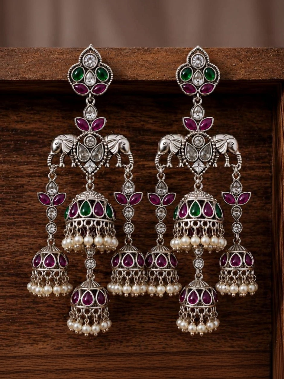 Pair of oxidised silver triple jhumka earrings displayed against dark wooden background showing stone and bell detail