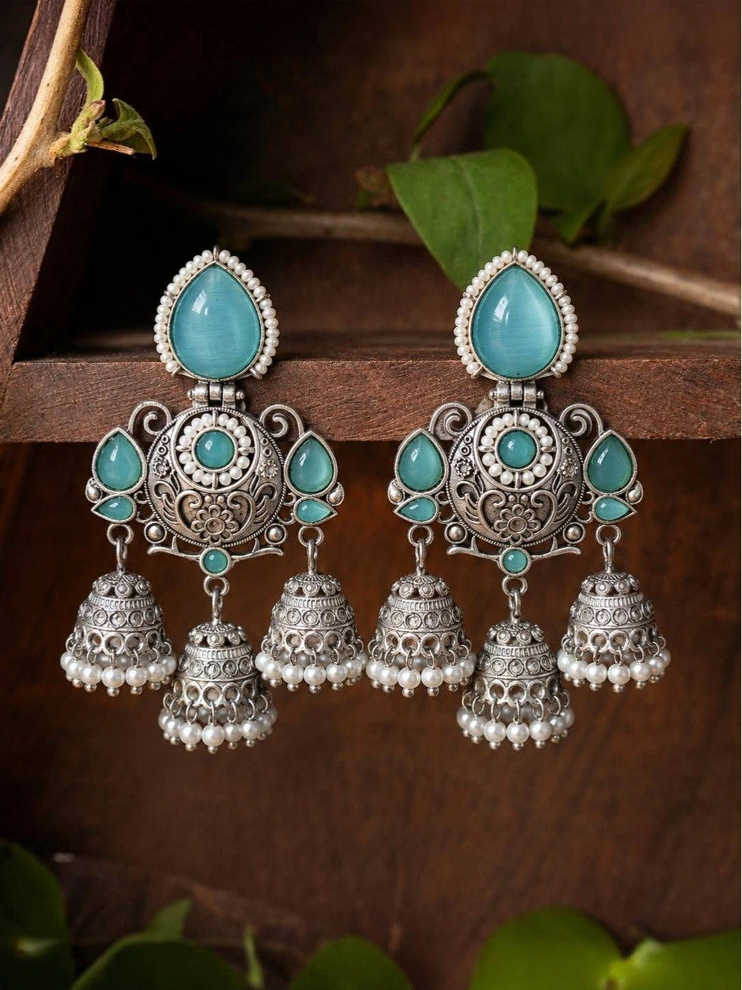 Two oxidised silver triple jhumka earrings displayed on a rustic wooden surface