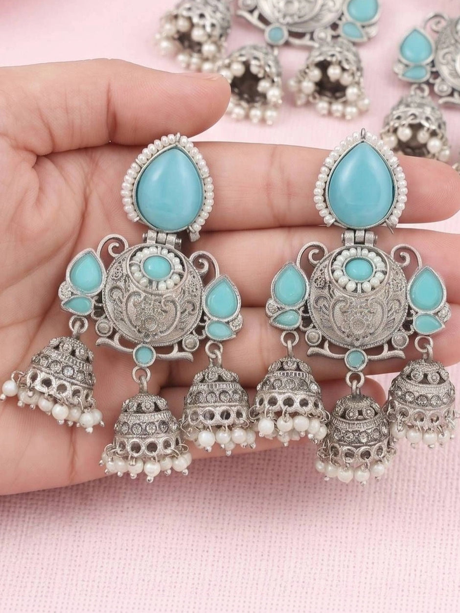 Hand holding a pair of oxidised silver triple jhumka earrings showing scale and detail