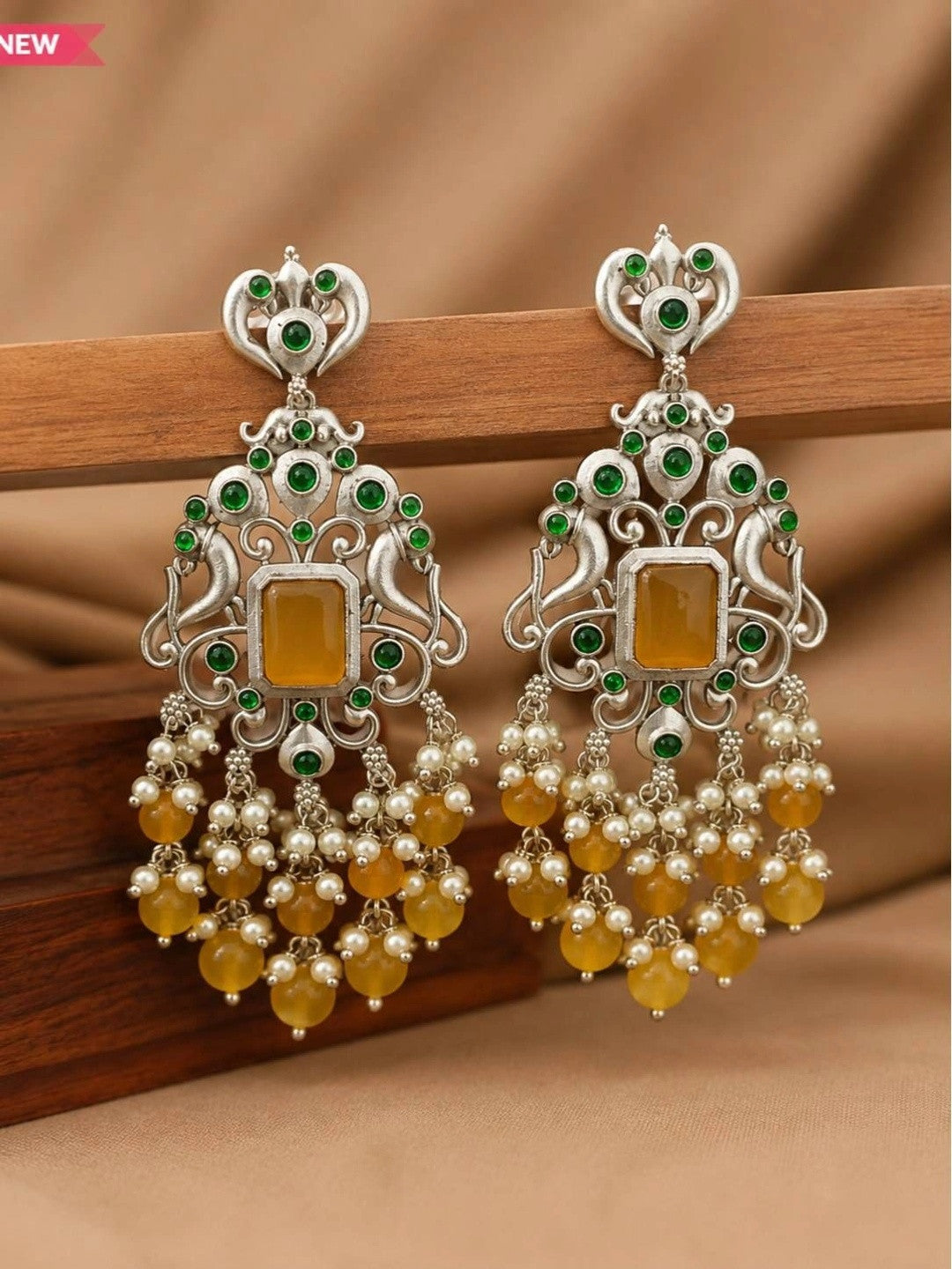 Pair of oxidised silver chandbali earrings resting on a wooden surface with yellow bead fringe