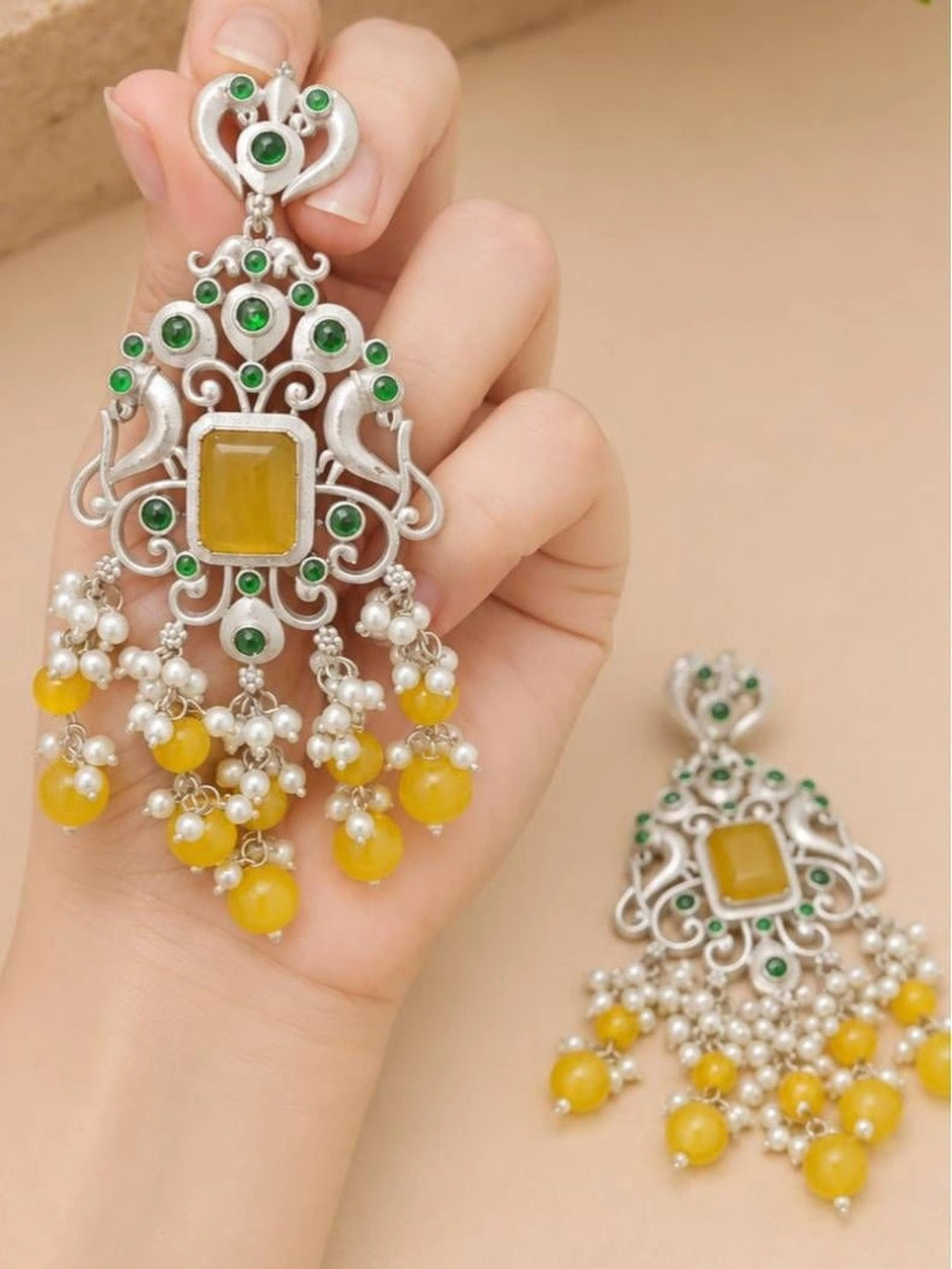 Close-up of oxidised silver chandbali earring held in hand showing peacock motif and yellow bead tassels