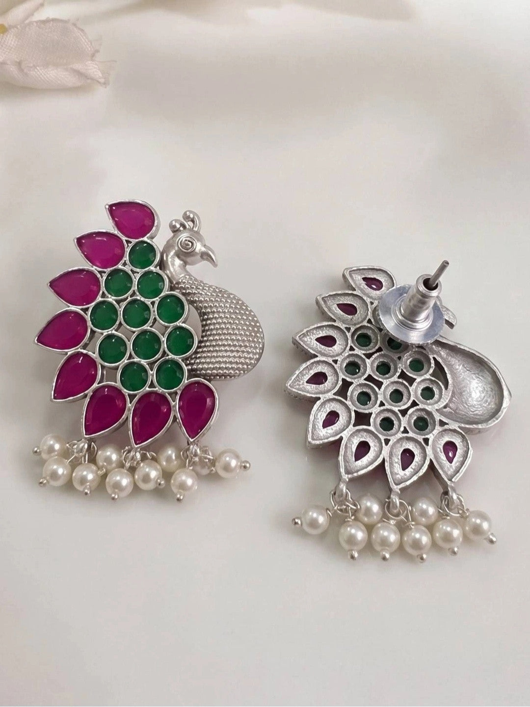 Front and back view of a single peacock stud earring on white fabric showing push-back fastening and stone setting