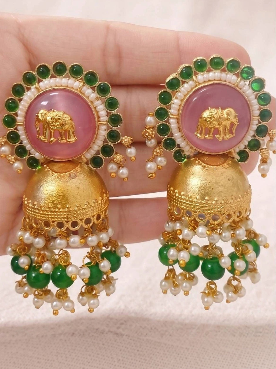 Two jhumkas held in hand showing pink cabochon elephant motif and layered green pearl fringe