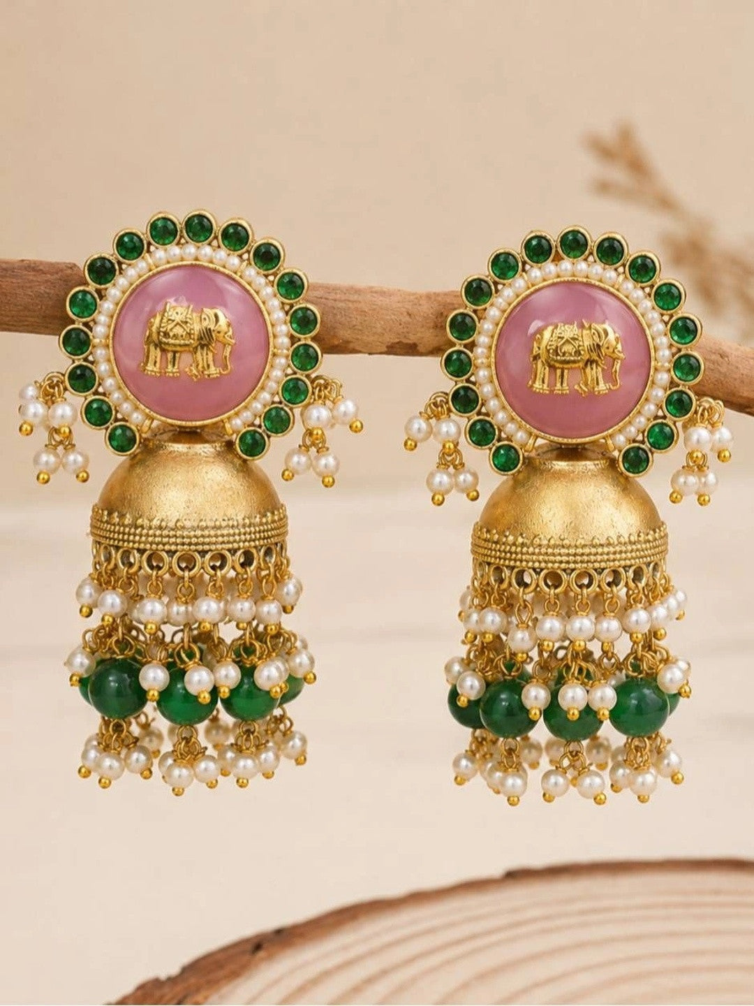 Pair of gold-plated jhumkas displayed on wooden prop showing filigree bell and bead fringe detail
